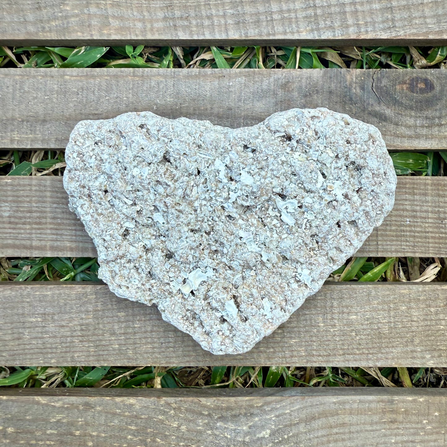 Heart-shaped stone on a wooden surface with grass in the background