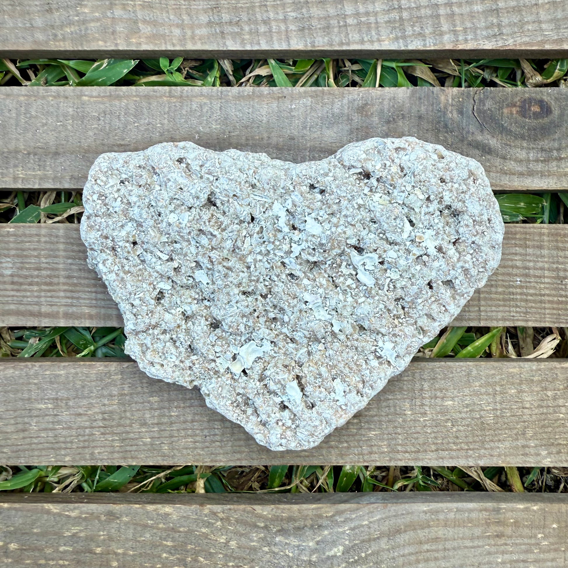 Heart-shaped stone on a wooden surface with grass in the background