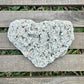 Heart-shaped stone on a wooden surface with grass in the background