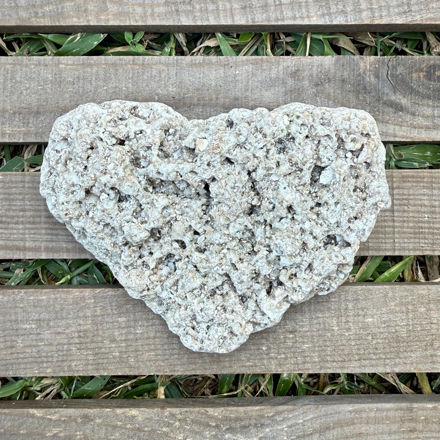 Heart-shaped stone on a wooden surface with grass in the background
