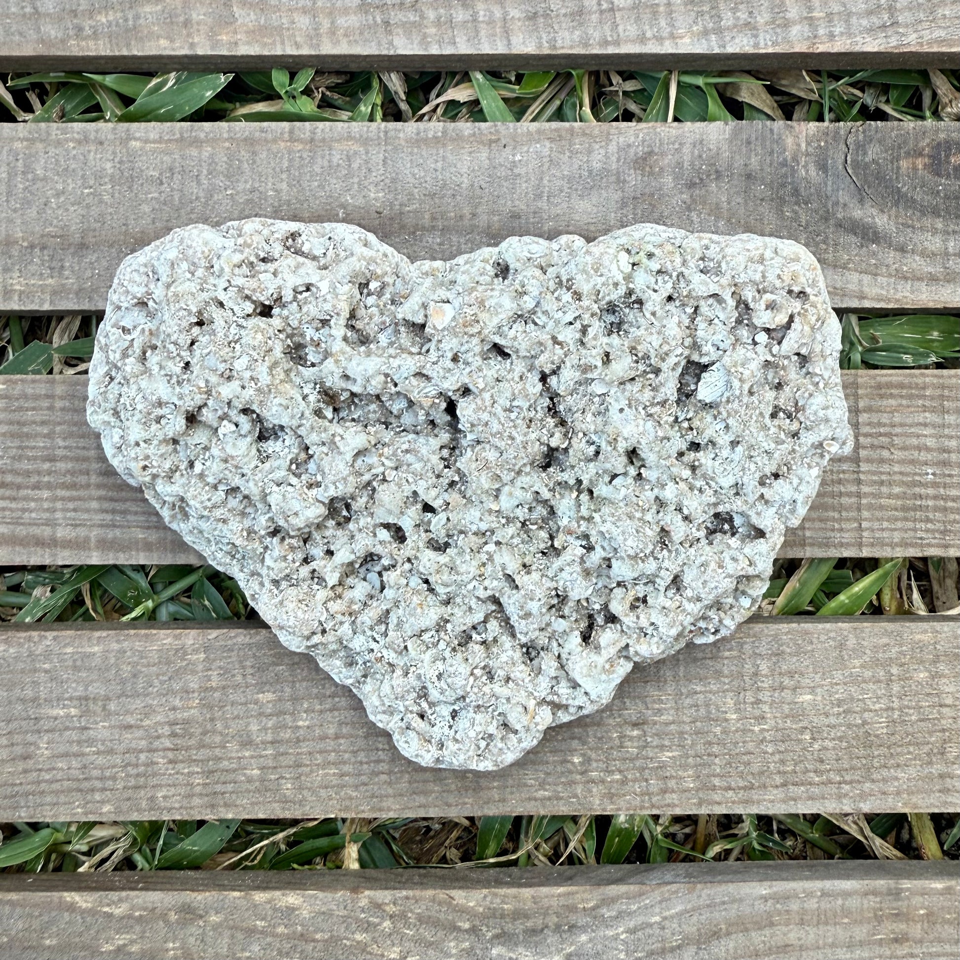 Heart-shaped stone on a wooden surface with grass in the background